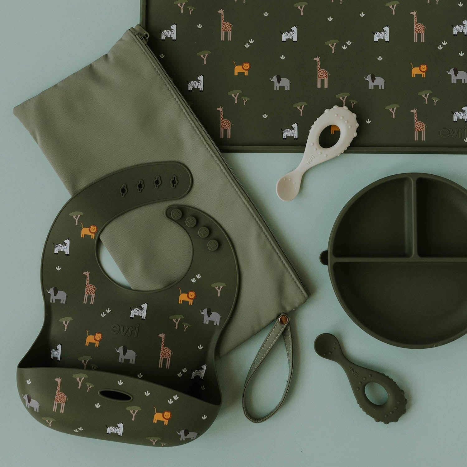 The Evrithing Bundle in evergreen featuring a matching silicone bib and placemat with a safari animal print, evergreen silicone divider plate, 2-pack silicone baby spoons, and matching wet dry pouch.