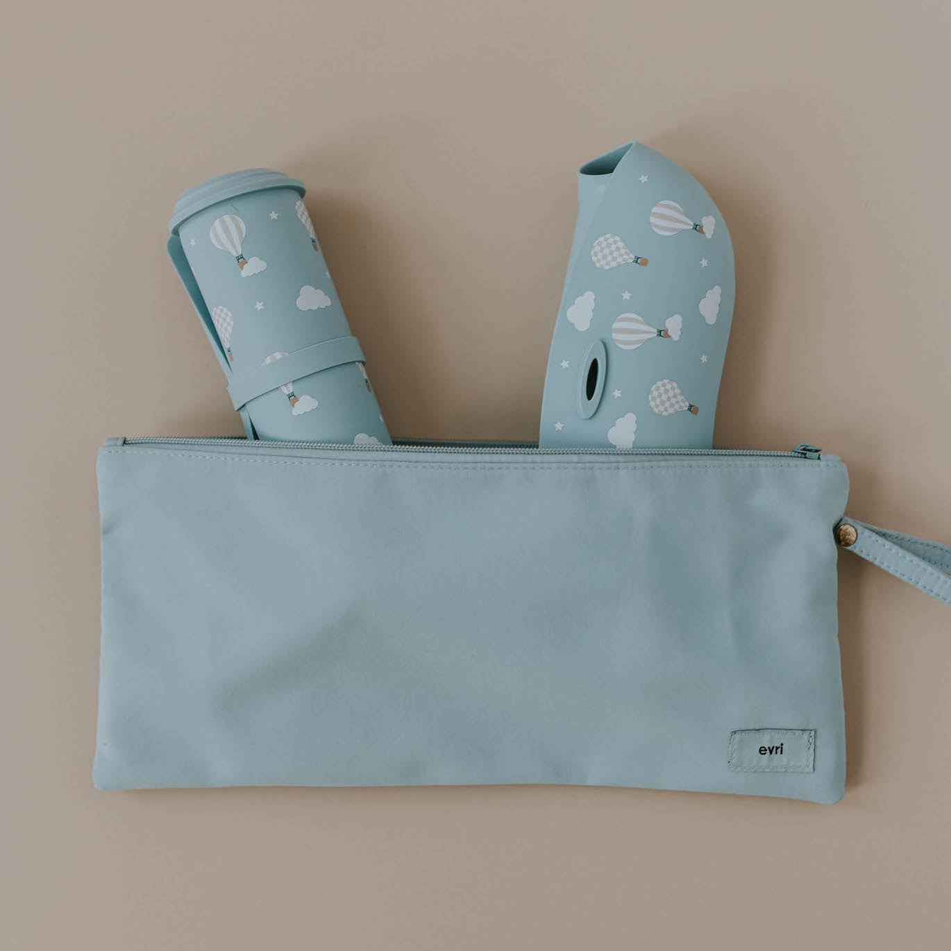 Various silicone feeding products spilling out of a sky blue wet dry pouch from the Evri brand. The items spilling from the pouch include a blue silicone bib and placemat that both feature a hot air balloon print.